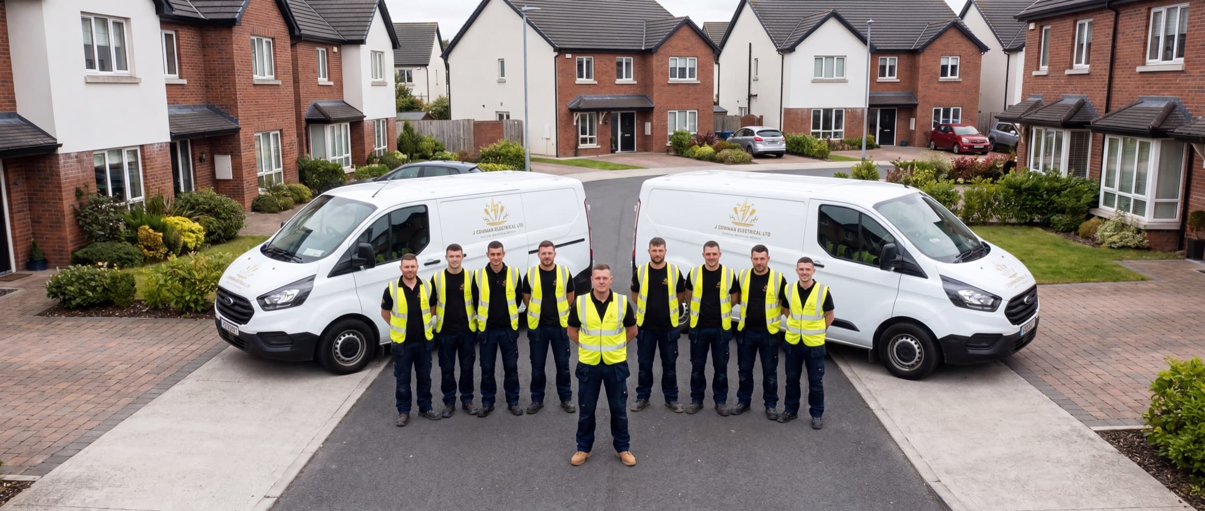 Jamie Cowman and the J Cowman Electrical Ltd 10-person crew in yellow hi-vis vests standing in front of two branded vans on a completed Leinster residential development