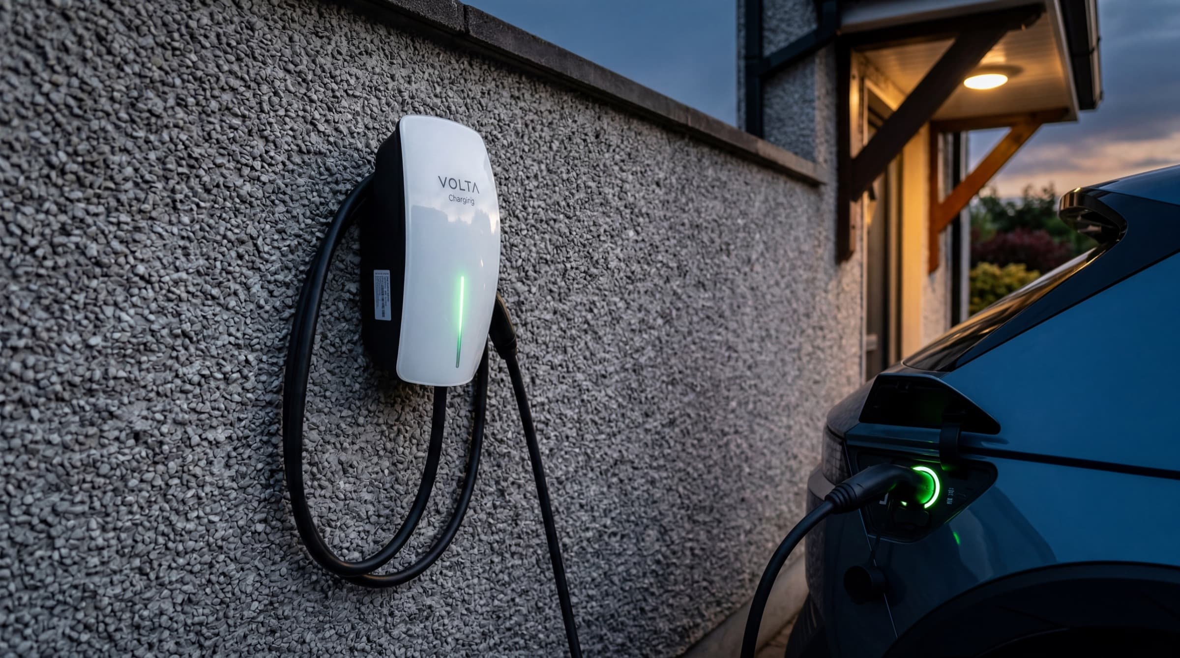 White wall-mounted residential EV charger with green LED strip glowing, cable plugged into an electric car on an Irish suburban driveway at dusk